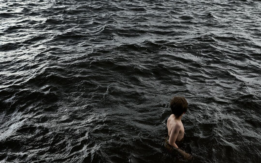 Ihminen seisoo järvessä, jossa vesi tummaa, melkein mustaa.