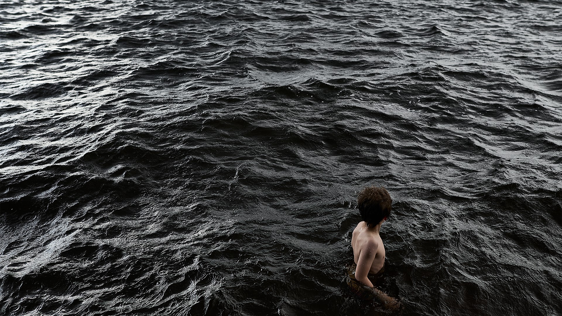 Ihminen seisoo järvessä, jossa vesi tummaa, melkein mustaa.