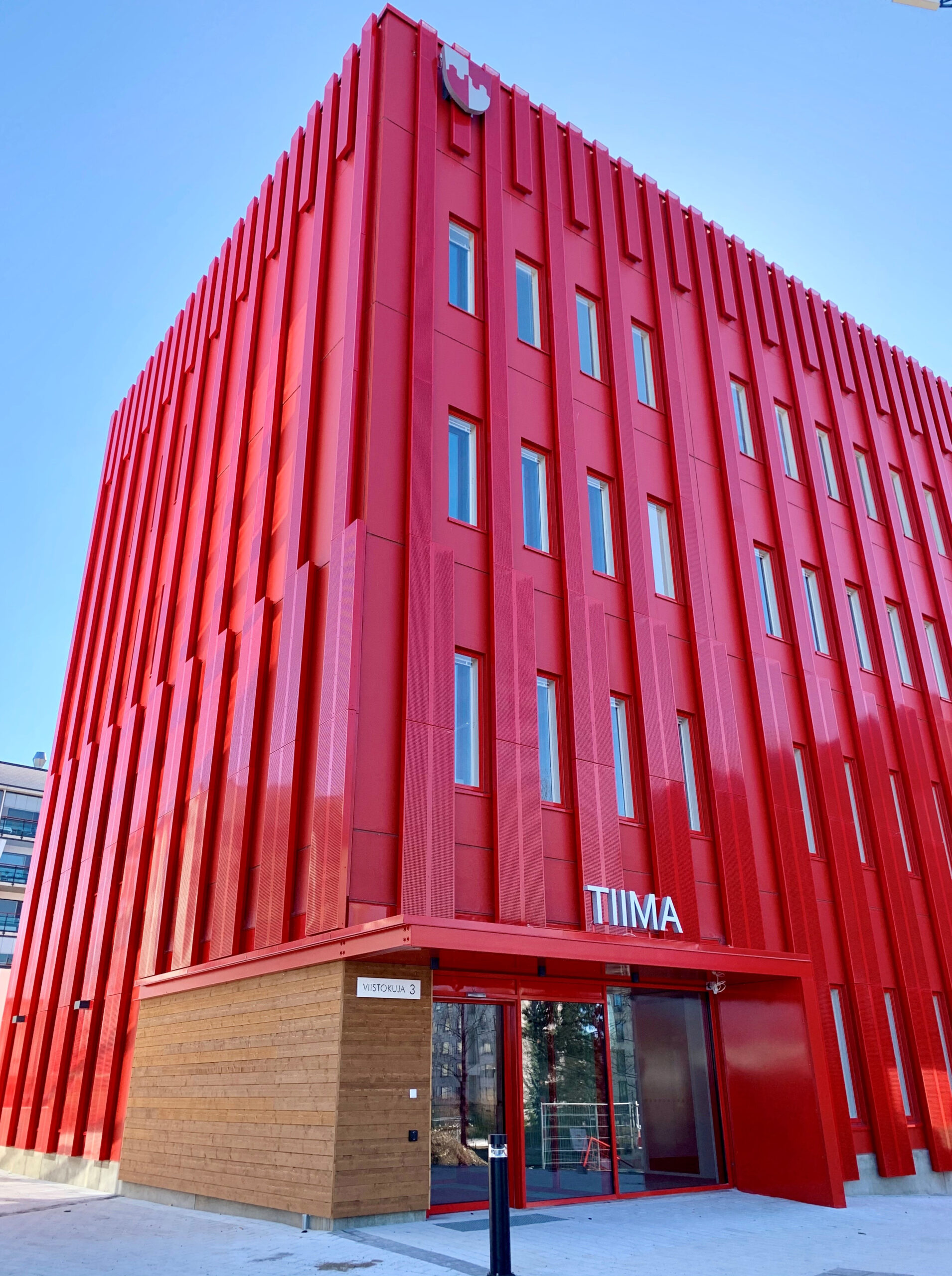 Uusi punainen nelikerroksinen toimitilarakennus, jonka yläosassa on kunnan vaakuna ja oven yläpuolella lukee valkoisin kirjaimin talon nimi Tiima.